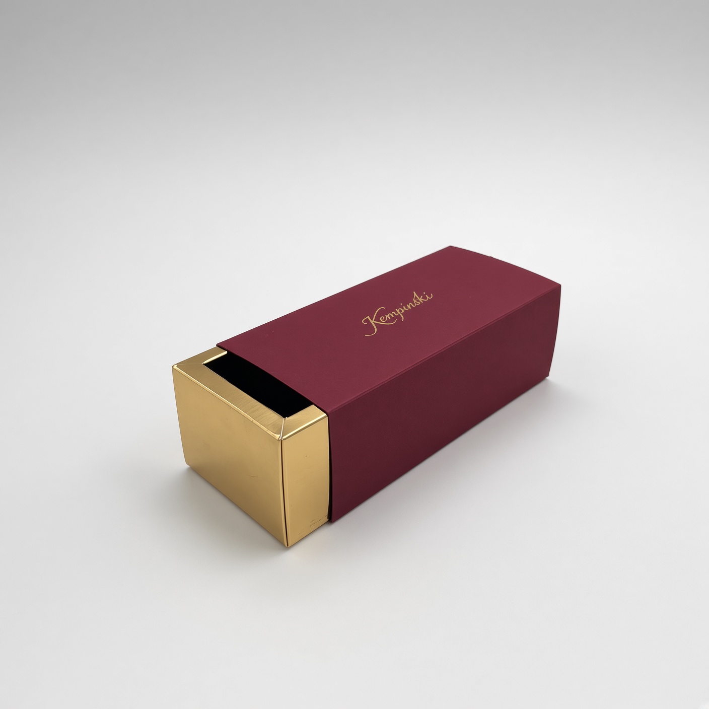 Bordo spalvos įmautė su aukso spalvos logotipu ir auksiniu ištraukiamu stalčiuku